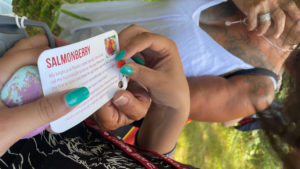 A student holds a card describing Salmonberry uses and identification with an instructor in front of greenery